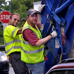 two men on back of garbage truck
